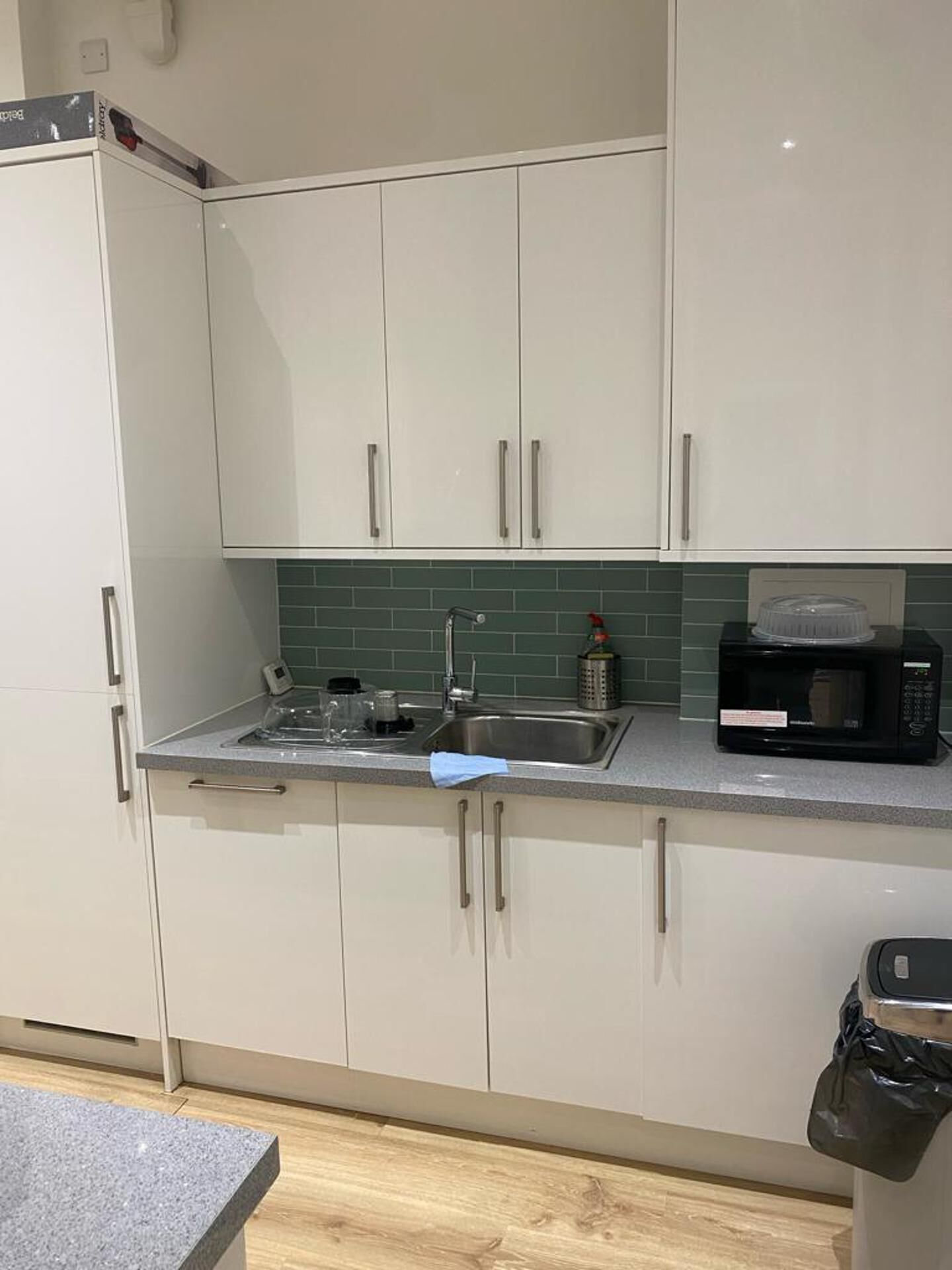A kitchen with white cabinets, a stainless steel sink, a microwave, and a trash bin.