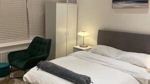A bedroom with a bed, a green chair, a wardrobe, a lamp, and a painting on the wall. - Stunning 1-bed Apartment in London (London)