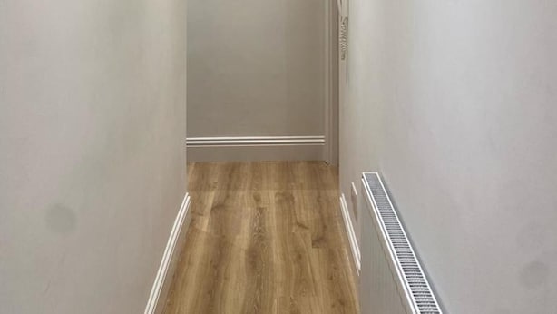 A narrow hallway with a wooden floor, white walls, and a small window with curtains. - Stunning 1-bed Apartment in London (London)