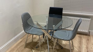A small, modern meeting room with a glass table and four grey chairs, a laptop on the table, and a radiator in the background. - Stunning 1-bed Apartment in London (London)