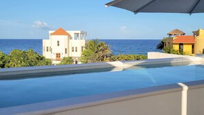 Ein Pool mit Meerblick, ein weißes Gebäude mit rotem Dach und ein gelbes Gebäude mit Strohdach.