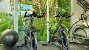 Zwei stehende Fahrräder in einem Fitnessstudio mit einem großen Trainingsball und einem Fenster mit Blick auf Grünflächen.