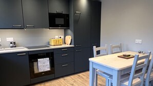 Une cuisine moderne avec des meubles de couleur sombre, un four à micro-ondes, un grille-pain et un coin repas comprenant une table et des chaises blanches.