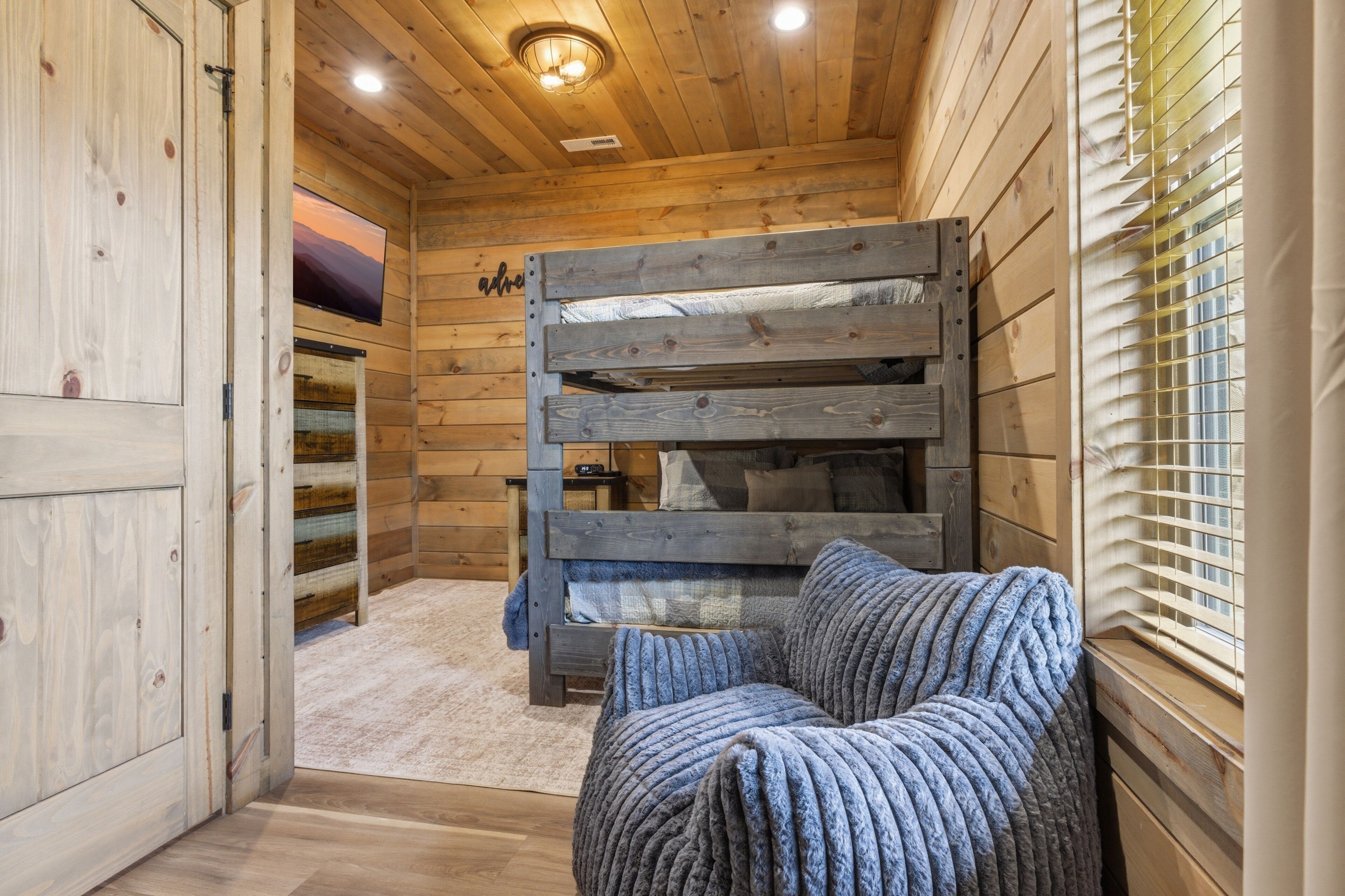 Ein Holzblockhaus Innenansicht mit Etagenbett, Fernseher und Fenster mit Jalousien.