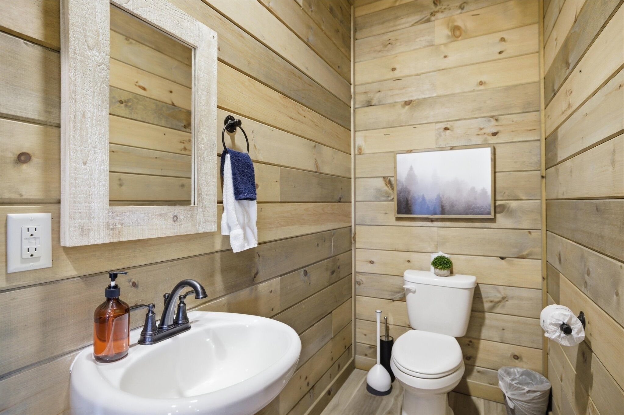 A wooden-paneled bathroom with a sink, mirror, toilet, and a small plant.