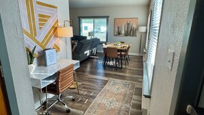 Un salon moderne avec un canapé, une table à manger et des chaises. On y trouve une lampe sur une table d’appoint, un tapis sur le sol et des œuvres d’art accrochées aux murs.