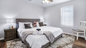 Ein Schlafzimmer mit Bett, Nachttischen, Deckenventilator, Fenster mit Jalousien und einem Sessel.