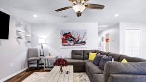 Ein modernes Wohnzimmer mit einem grauen Ecksofa, einem Holztisch, einer Stehlampe und einem Deckenventilator.