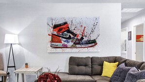 Ein Wohnzimmer mit grauem Sofa, einem kleinen weißen Beistelltisch, einer Lampe und einer Vase mit Blumen.