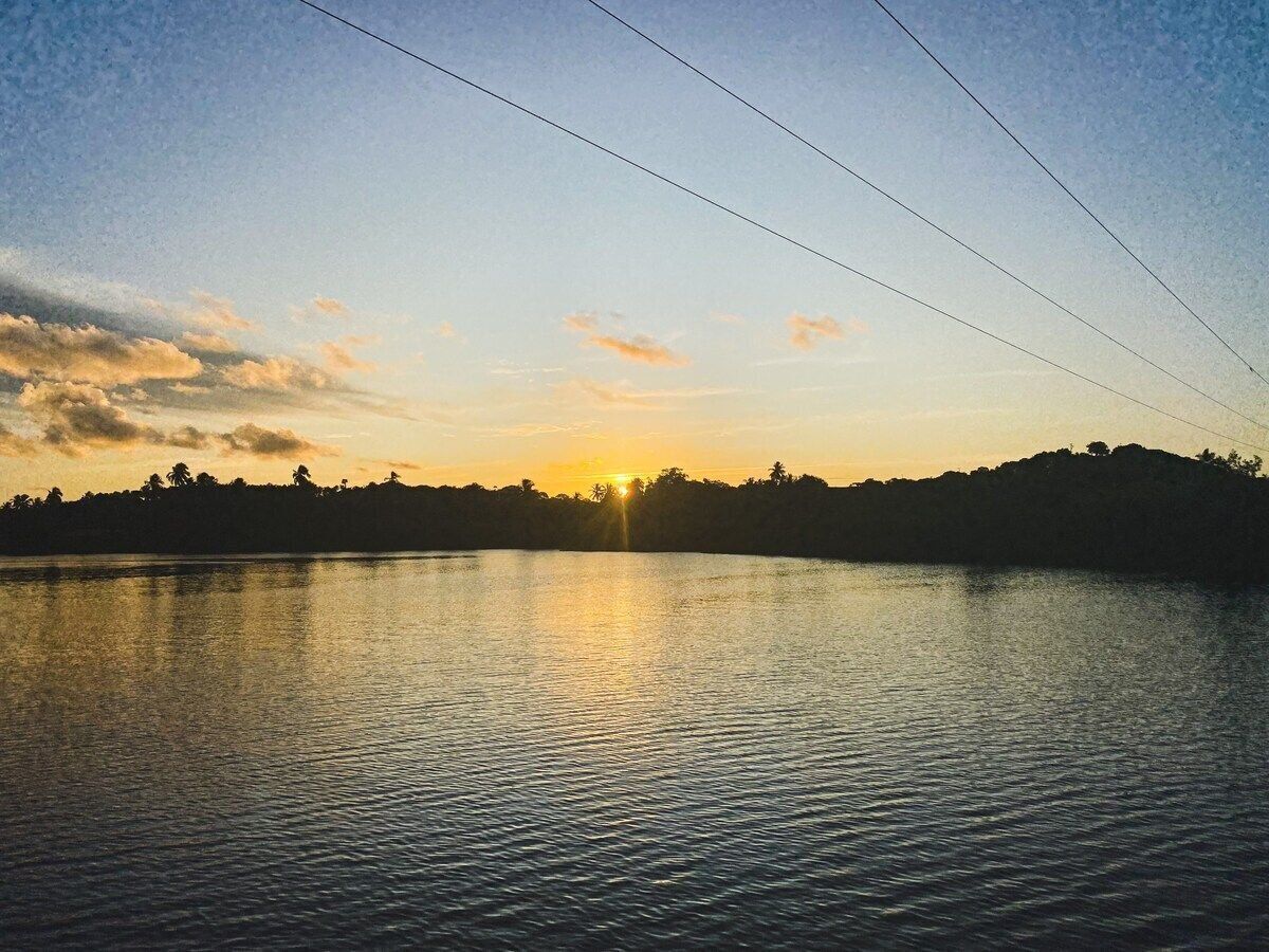 A calm lake at sunset with a silhouette of trees and a clear sky.