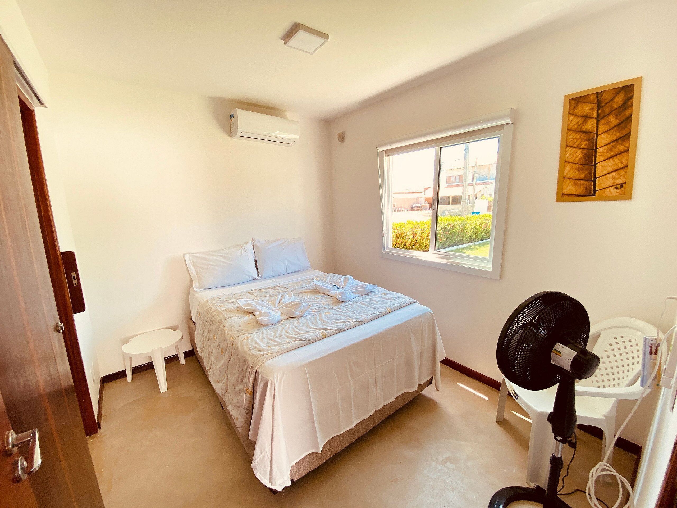 A bedroom with a bed, a standing fan, a window, and a door.