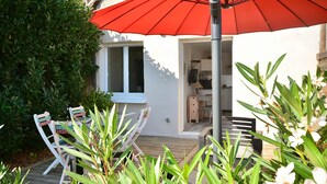 A patio area with a red umbrella, white chairs, and a wooden deck.