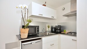 A modern kitchen with white cabinets, a black countertop, a built-in dishwasher, a coffee maker, and a gas stove.