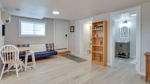 Une pièce comprenant une table à manger, des chaises, un canapé bleu, une bibliothèque en bois et une petite salle de bain avec un miroir et un lavabo.