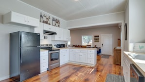 Una cocina amplia con muebles blancos, un refrigerador negro, piso de madera y una isla grande con un lavamanos.