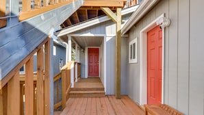 Una terraza de madera con una puerta roja y un banco.