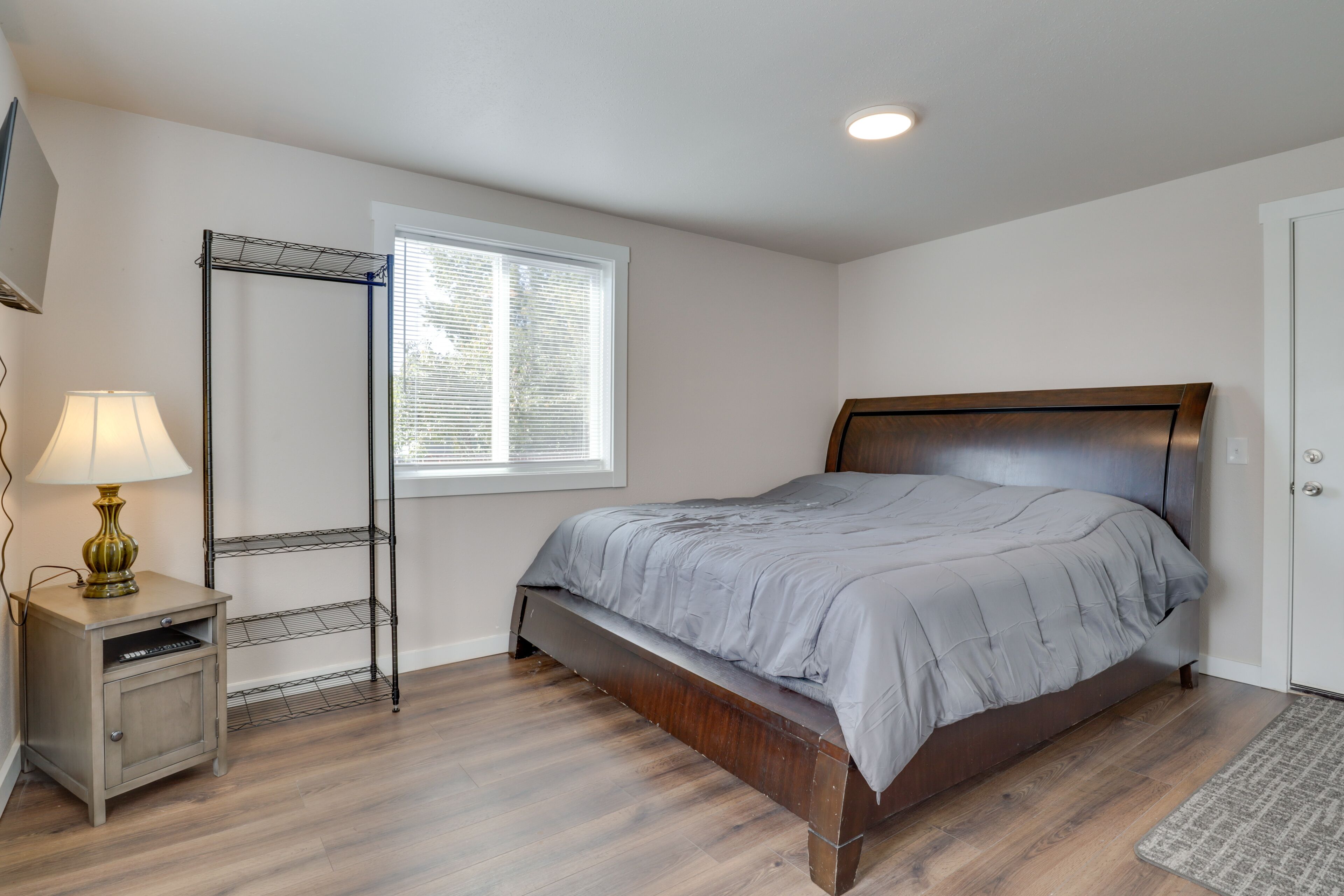 Un dormitorio con una cama, una mesita de noche, una lámpara, una ventana y una puerta.