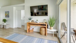 A modern living room with a wooden desk, a flat-screen TV, and a comfortable seating area with a chair and ottoman. - Sunny St Pete Getaway With Shared Pool & Hot Tub (St. Petersburg)