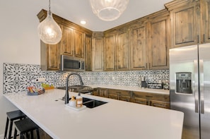 A kitchen with wooden cabinets, a stainless steel refrigerator, a microwave, a coffee maker, and a sink with a modern faucet. - Brian Head Retreat w/ Deck, Shuttle to Ski Slopes! (Brian Head)