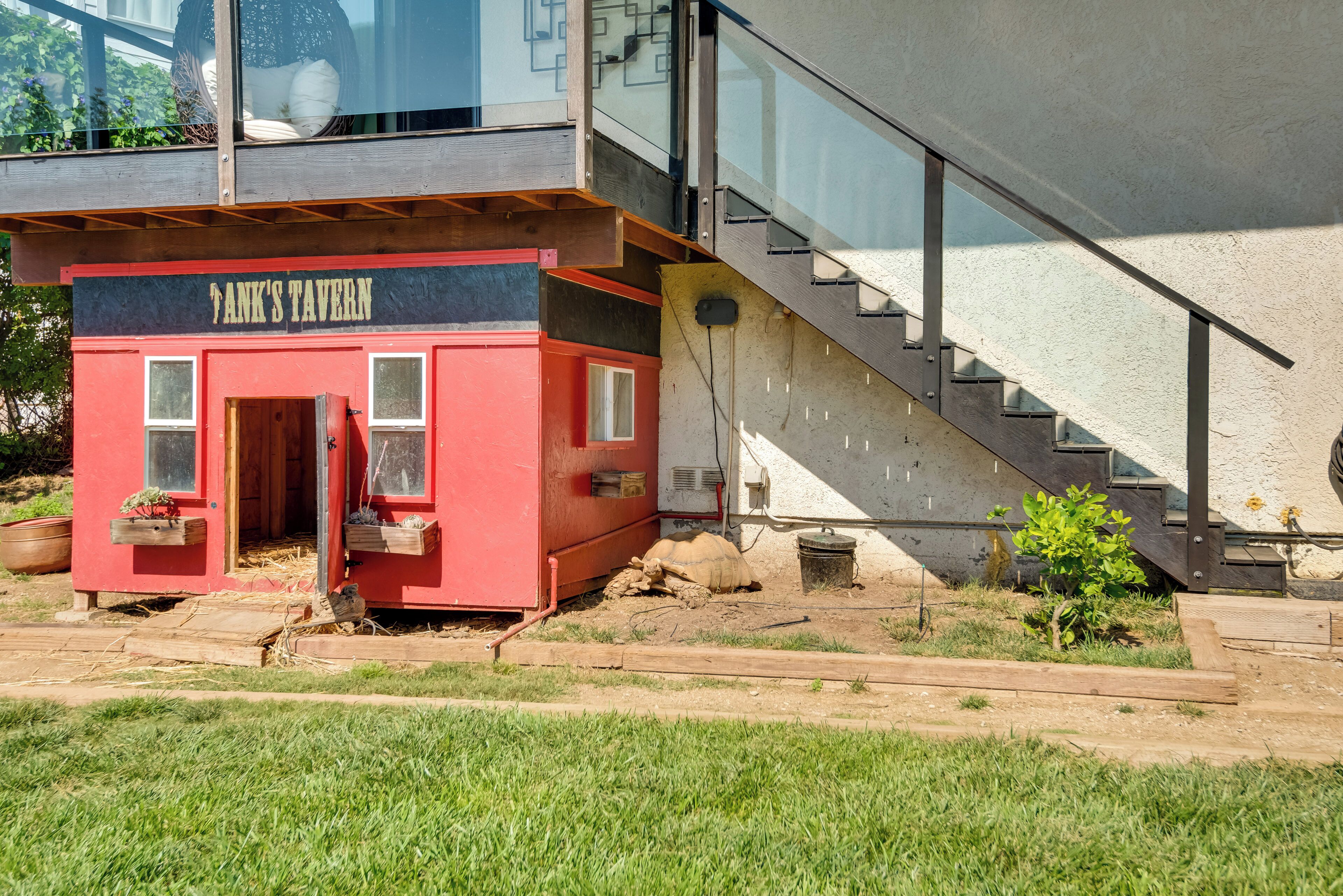 Um edifício vermelho com uma placa que diz "Tank's Tavern". Possui um deck de madeira e uma escadaria que leva a um segundo andar.