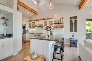Uma cozinha moderna com armários brancos, uma ilha central e luminárias pendentes.