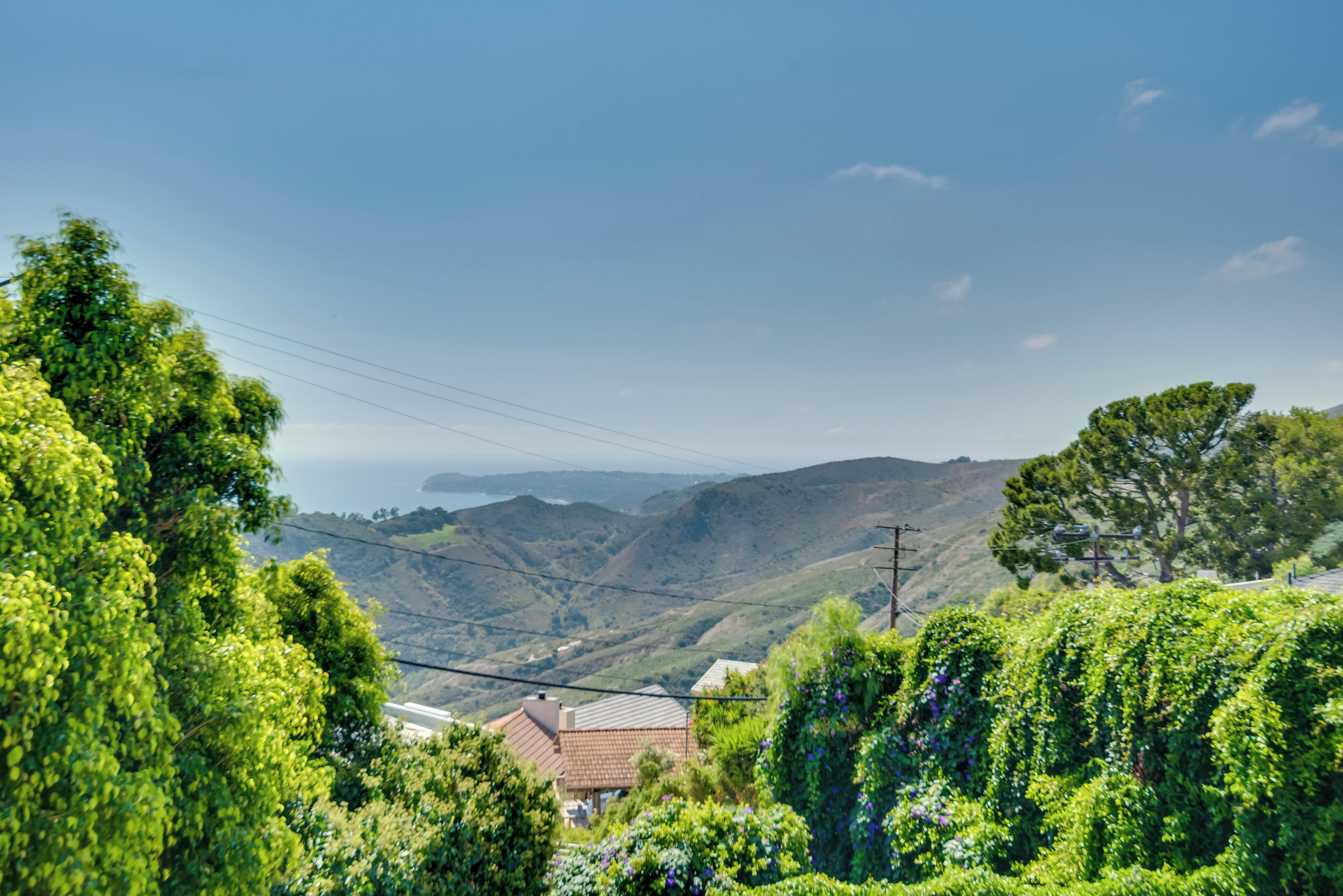 A hillside view with a house, power lines, and distant mountains.