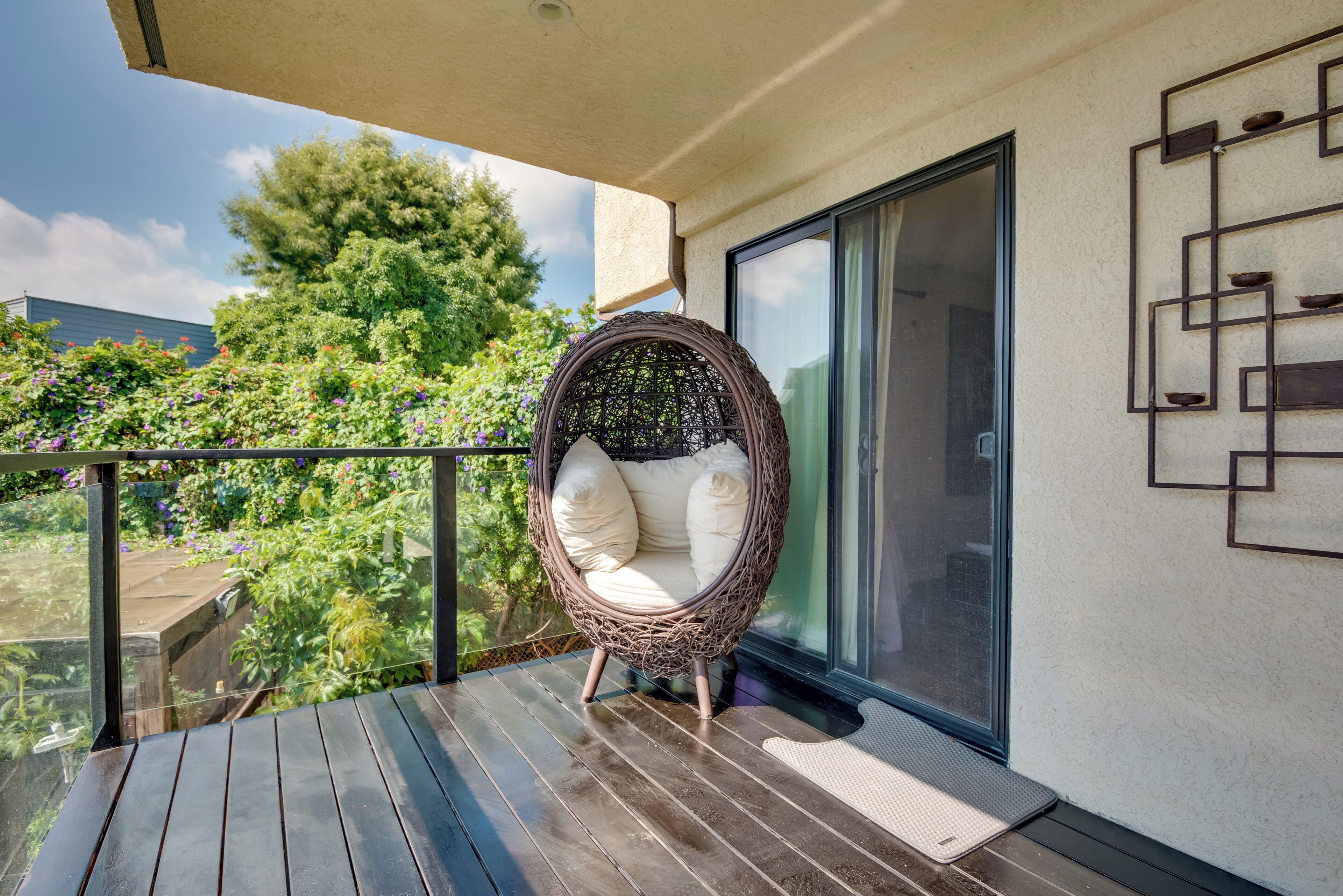 A wicker chair on a wooden deck with a glass door and a view of greenery.
