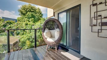 A wicker chair on a wooden deck with a glass door and a view of greenery.