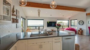 A modern kitchen with a large island, wooden beams, and a view of the outdoors.