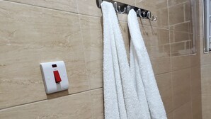 Une salle de bain avec des murs carrelés de couleur beige, un porte-serviettes blanc avec deux serviettes et un interrupteur rouge.