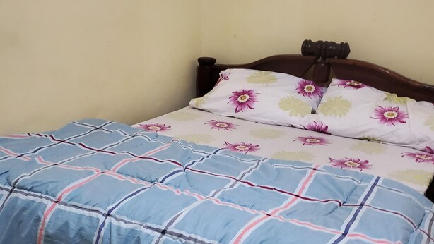 Un lit avec une couvre-lit à carreaux bleus et rouges, une tête de lit en bois et deux oreillers à motifs floraux.