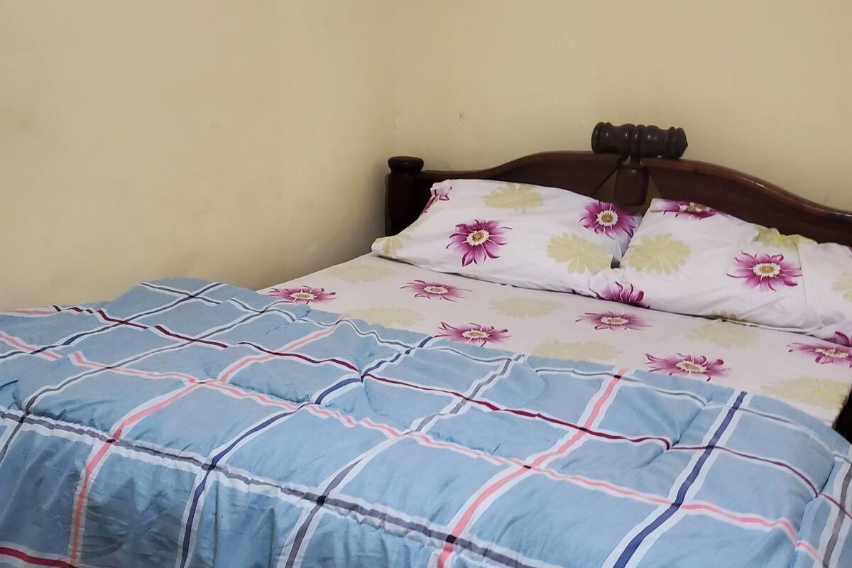 A bed with a blue and red plaid bedspread, a wooden headboard, and two pillows with a floral pattern.