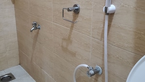 Une salle de bain avec des murs carrelés de couleur beige, une douche avec un pommeau de douche amovible, un robinet amovible et des toilettes.