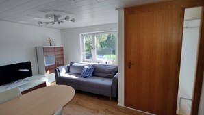 Un salon moderne avec un canapé, un téléviseur, un meuble en bois et une grande fenêtre.