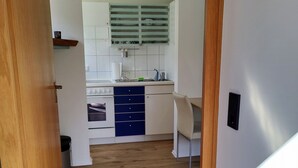 Un couloir étroit mène à une cuisine équipée de meubles blancs, d’une cuisinière et d’un évier.