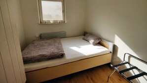Une petite chambre avec un lit simple, une fenêtre, un radiateur et une chaise.