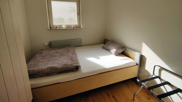 Une petite chambre avec un lit simple, une fenêtre, un radiateur et une chaise.
