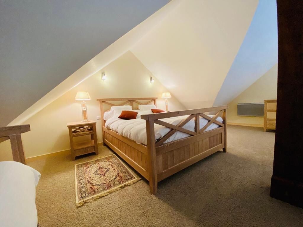A bedroom with a sloped ceiling, a wooden bed, two bedside tables with lamps, and a patterned rug.