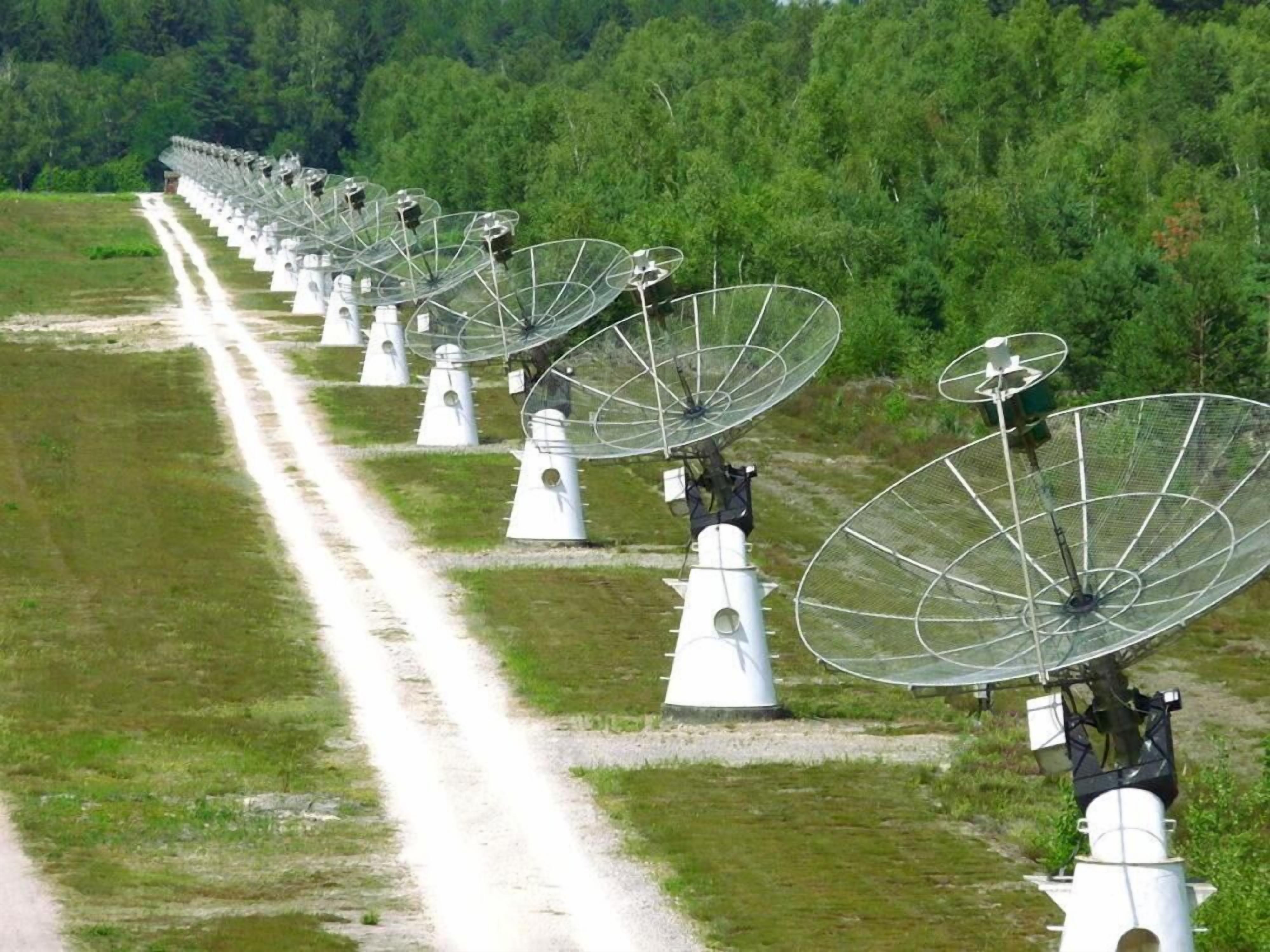 A series of large satellite dishes aligned in a row on a grassy field.
