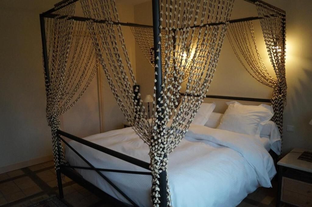 A four-poster bed with a canopy made of hanging chains, a bedside table, and a lamp.