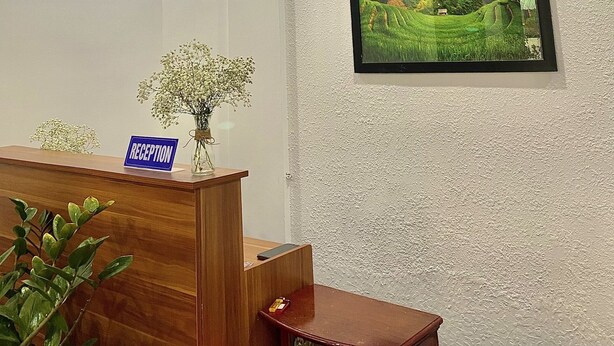 A reception area with a wooden desk, a 'RECEPTION' sign, a framed landscape picture on the wall, and a ceiling with recessed lighting. - Shine Homestay Hue (Hue)