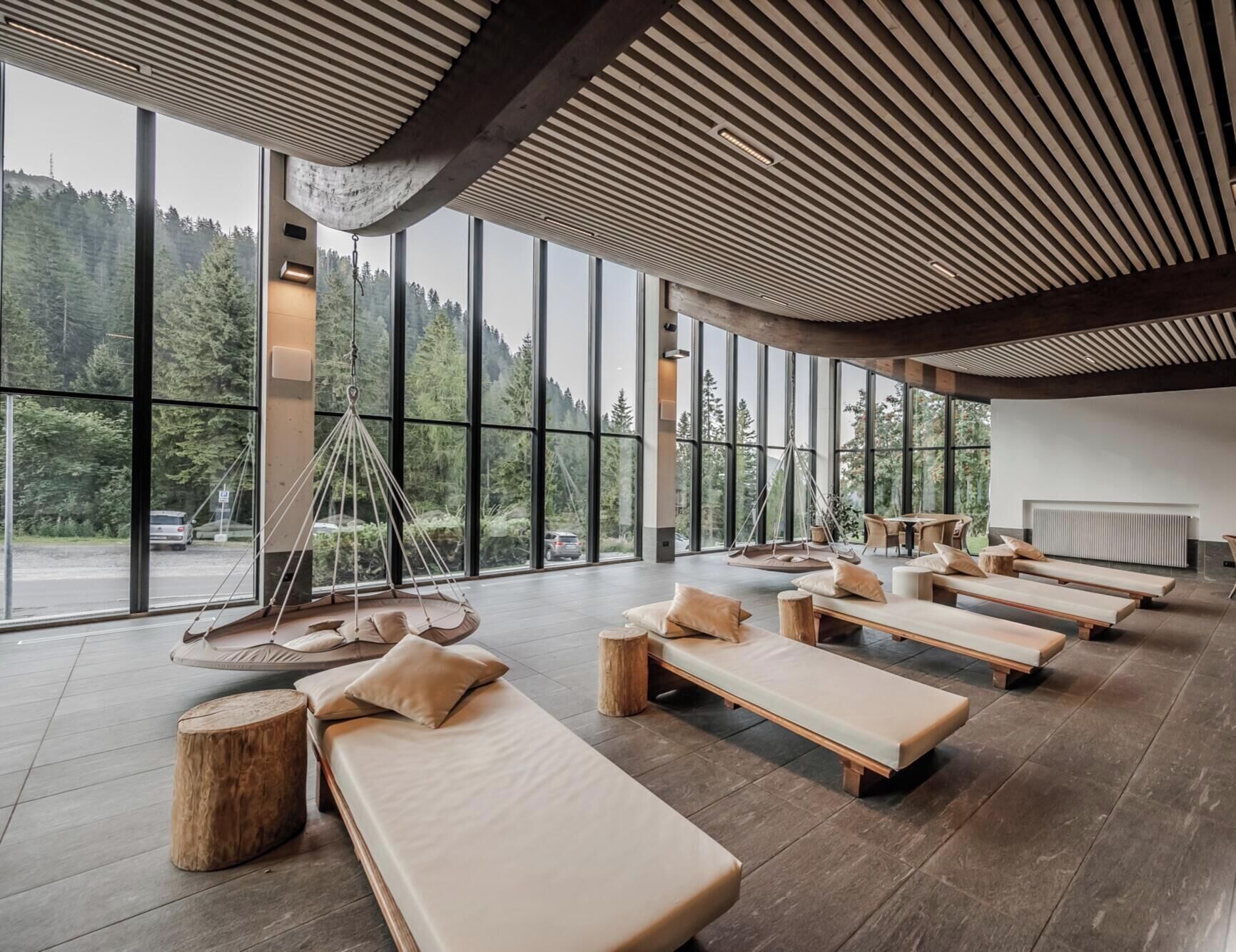 A modern spa room with large windows, wooden loungers, and a hanging chair.