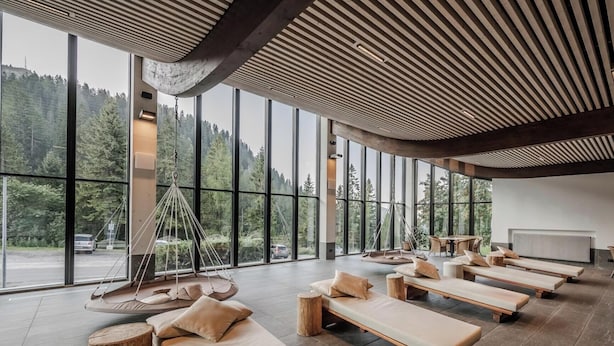A modern spa room with large windows, wooden floors, and multiple lounge areas. - HOTIDAY Apartment Collection - Campiglio Grostè (Pinzolo)