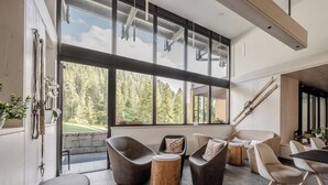 A modern interior with large windows, a stone wall, and a mix of seating options including chairs and a bench. - HOTIDAY Apartment Collection - Campiglio Grostè (Pinzolo)