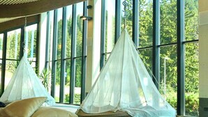 A room with large windows, two hanging beds with sheer curtains, and a wooden bench. - HOTIDAY Apartment Collection - Campiglio Grostè (Pinzolo)