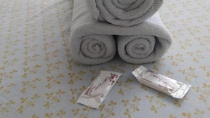 A bed with a floral-patterned bedspread and three rolled gray towels stacked on top of each other. - hotel minas salvador (Salvador)