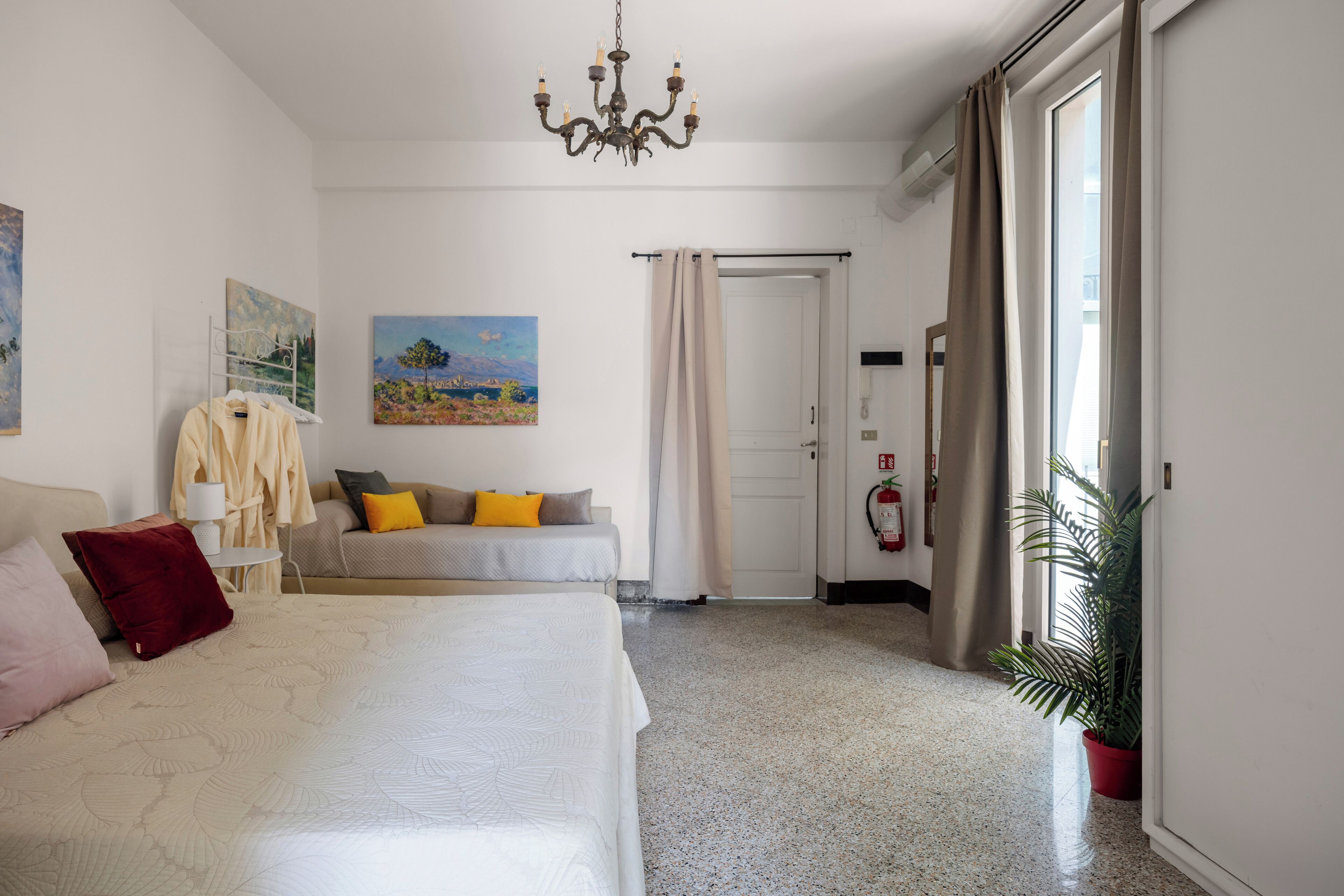 Hotelkamer met een bed, een slaapbank, een kroonluchter, een schilderij, een plant en een deur met gordijn.