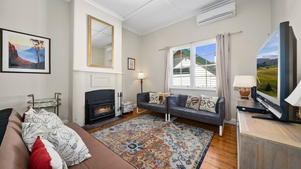 A cozy living room with a fireplace, a sofa, a television, and a large window with curtains.