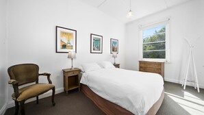 A bedroom with a bed, a chair, a nightstand, a dresser, and a window.