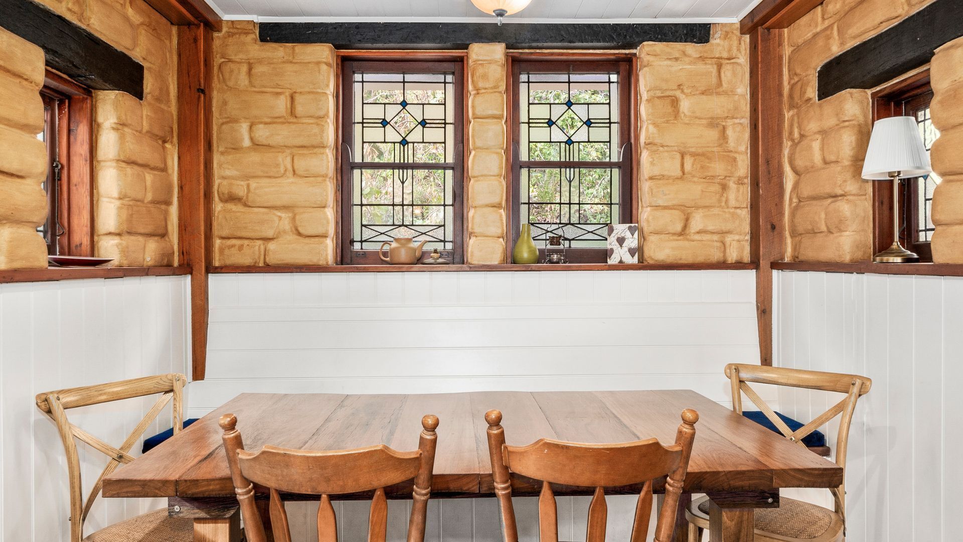 A rustic dining room with a wooden table and chairs, stone walls, and a window with decorative glass panes.